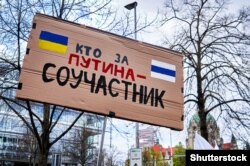 Плакат російською мовою «Хто за Путіна – той співучасник» на демонстрації проти війни Росії в Україні, Ганновер, Німеччина, 9 квітня 2022 року