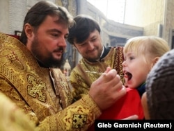 Митрополит Переяславський і Вишневський, архієрей Православної церкви України (ПЦУ) Олександр (Драбинко) (ліворуч) причащає дівчинку у Спасо-Преображенському храмі Києва.