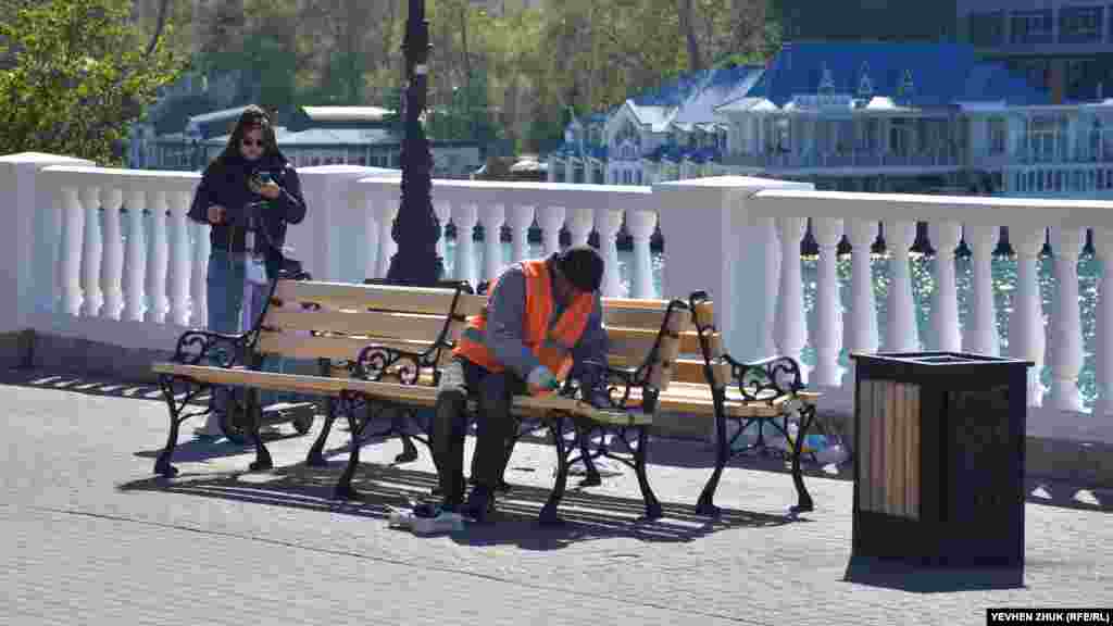 Працівник фарбує металеві частини лавки