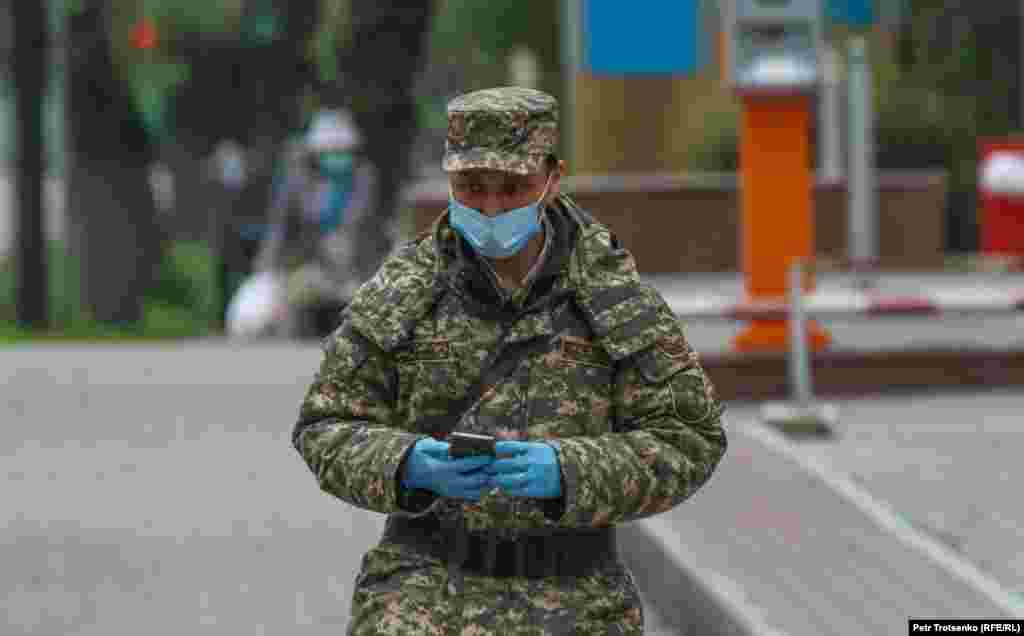 Бетіне медициналық маска тағып, қолына арнайы қолғап киіп алған әскери қызметкер.