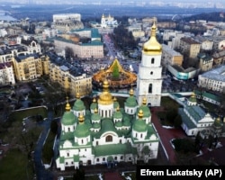 У Києві до новорічно-різдвяних свят підготували спеціальний маршрут, який з'єднав три локації. На кожній з них є своя новорічна ялинка. Локації облаштовані на Софійській і Контрактовій площах, а також біля Арки дружби народів. На фото на передньому плані Софійський собор – пам’ятка української архітектури і монументального живопису, споруда часів України-Русі (1011 рік). Одна з найголовніших християнських святинь Східної Європи, історичний центр Київської митрополії. Ансамбль Софійського монастиря занесено до спадщини ЮНЕСКО